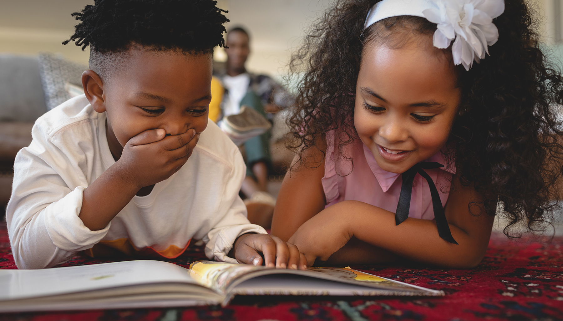 Front view of cute African American sibling lying on floor and reading a storybook in a comfortable home. Social distancing and self isolation in quarantine lockdown for Coronavirus Covid19